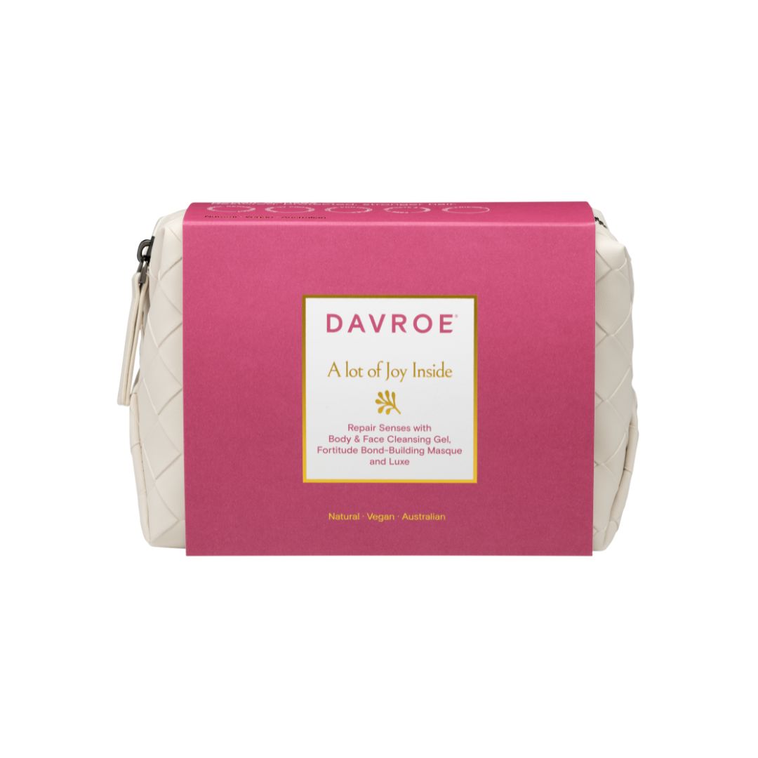A Davroe white quilted cosmetic pouch with a bright pink paper sleeve wrapped around it, shown on a plain white background.