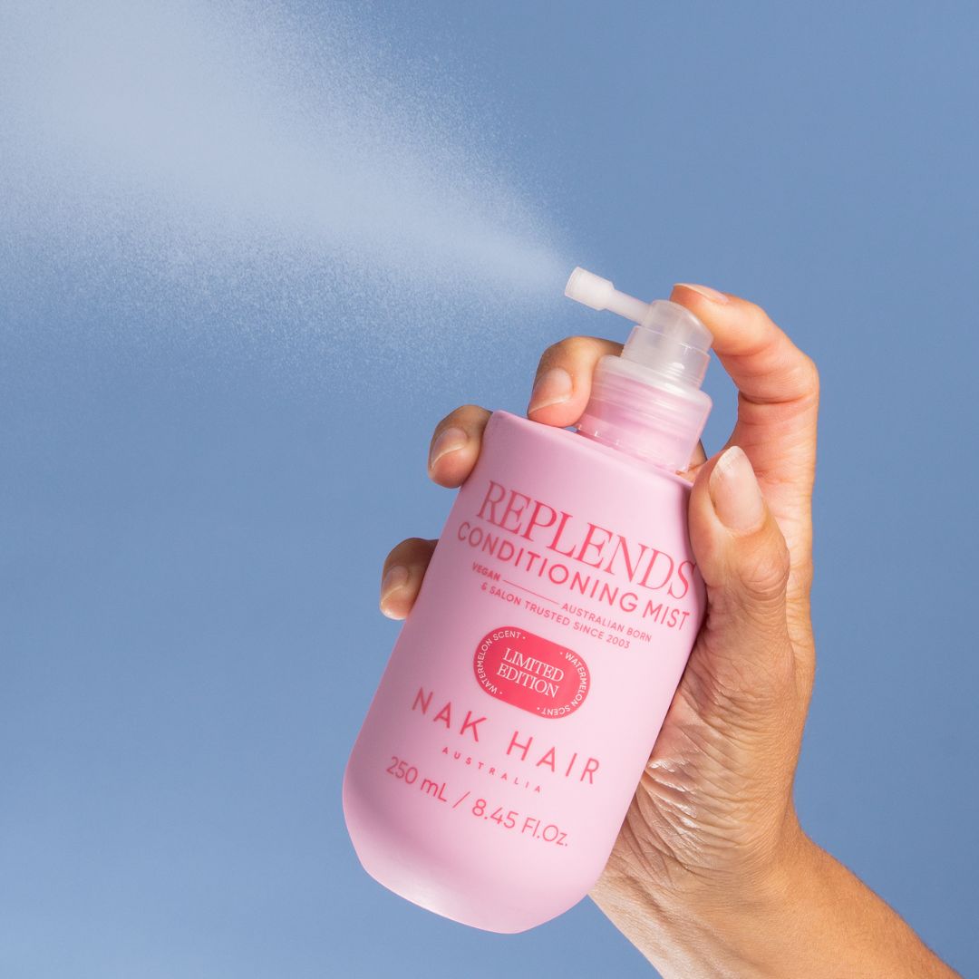 Hand holding a pink bottle of Replends Conditioning Mist against a blue background
