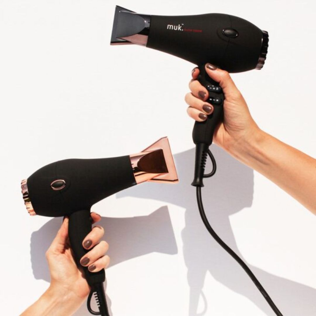Two black hair dryers with rose gold accents held by hands on a white background