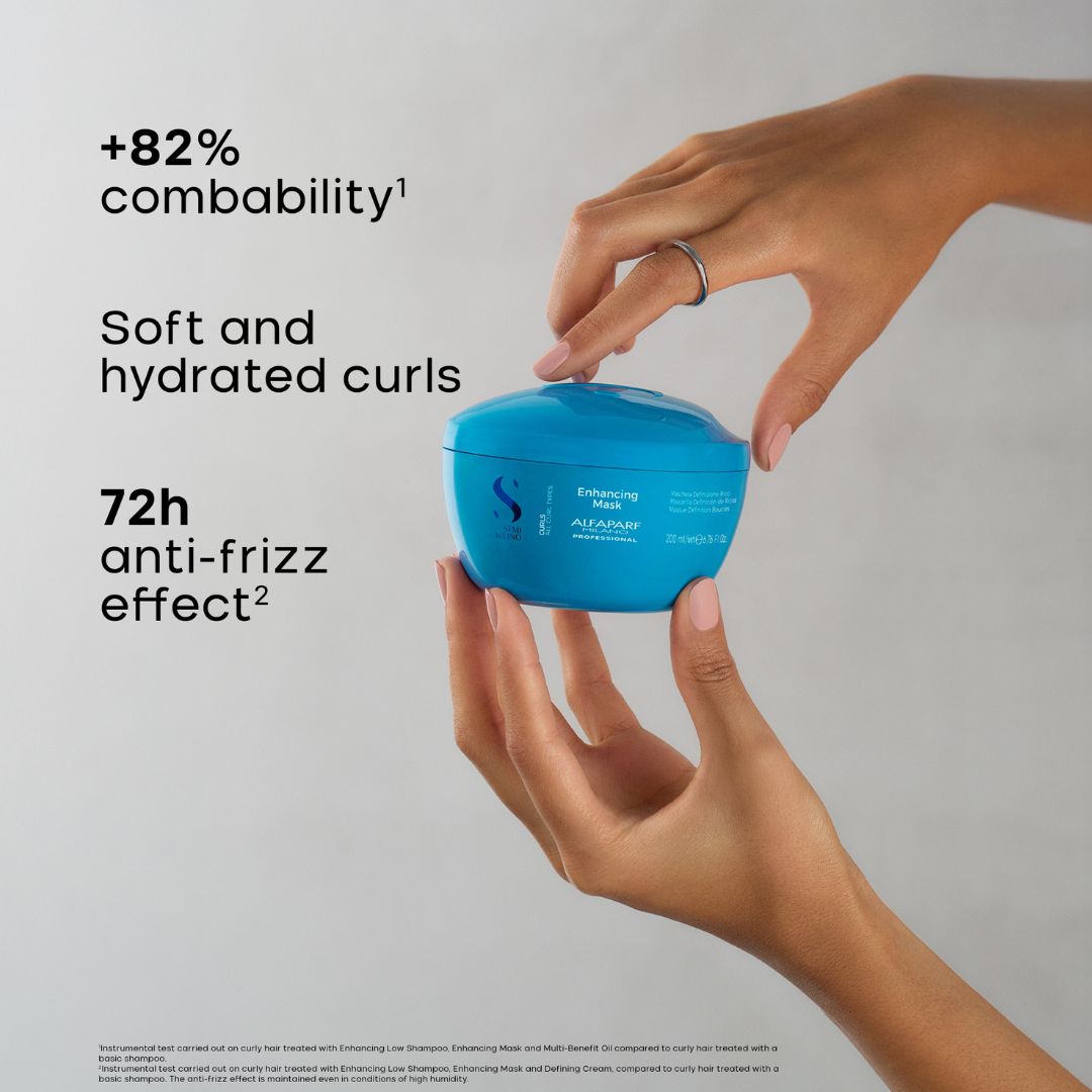 A person's hands holding a blue jar of Schwarzkopf Alchemist Enhancing Hair, with text on the left highlighting '+82% combability', 'Soft and hydrated curls', and '72h anti-frizz effect'.