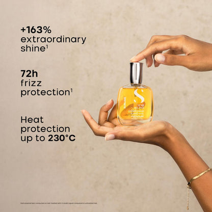 A hand holds a square glass bottle of hair oil with a silver cap, while another hand touches the top. The bottle contains a golden-yellow liquid and has white text including an 'S' logo.