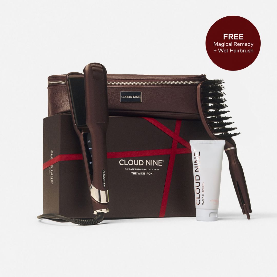 Cloud Nine hair styling set on a light gray background, featuring a brown flat iron, hairbrush, hair wrap tool, zippered case, and a white tube of hair remedy, with a brown circular badge reading 'FREE Magical Remedy + Wet Hairbrush'.