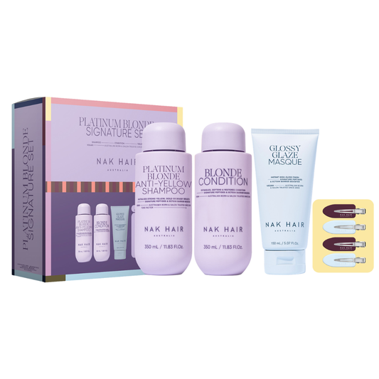 Nak Hair Platinum Blonde Signature Set hair care gift set, featuring a lavender and gold box, two lavender bottles of shampoo and conditioner, a white tube of gloss hair masque, and a yellow card with three mini hair clips, all on a white background.