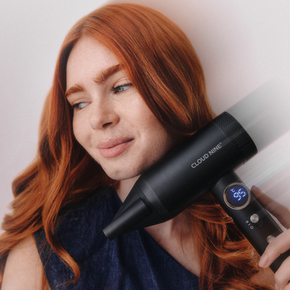 A woman with long red hair holds a black Cloud Nine hair dryer against her hair, with a white mist effect indicating airflow. The hair dryer has a digital temperature display showing 36 degrees Celsius.