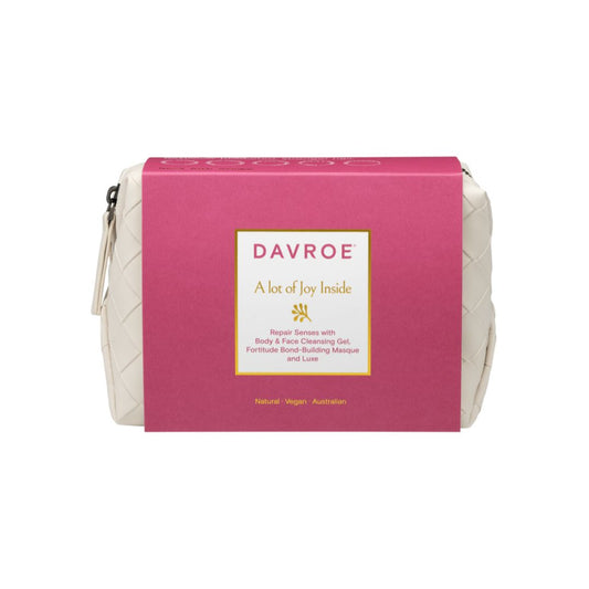 A Davroe white quilted cosmetic pouch with a bright pink paper sleeve wrapped around it, shown on a plain white background.