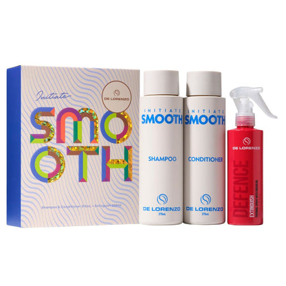 De Lorenzo Initiate Smooth haircare set including a colorful gift box, a white shampoo bottle, a white conditioner bottle, and a red defence spray bottle on a white background.