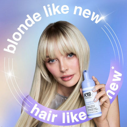 Woman with blonde hair holding a K18 hair product against a gradient blue background