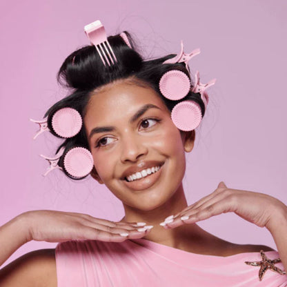 Woman with pink hair rollers against a pink background