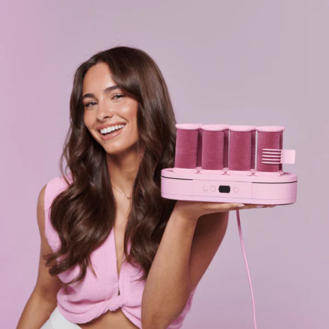 Woman holding a pink hair styling tool against a pink background