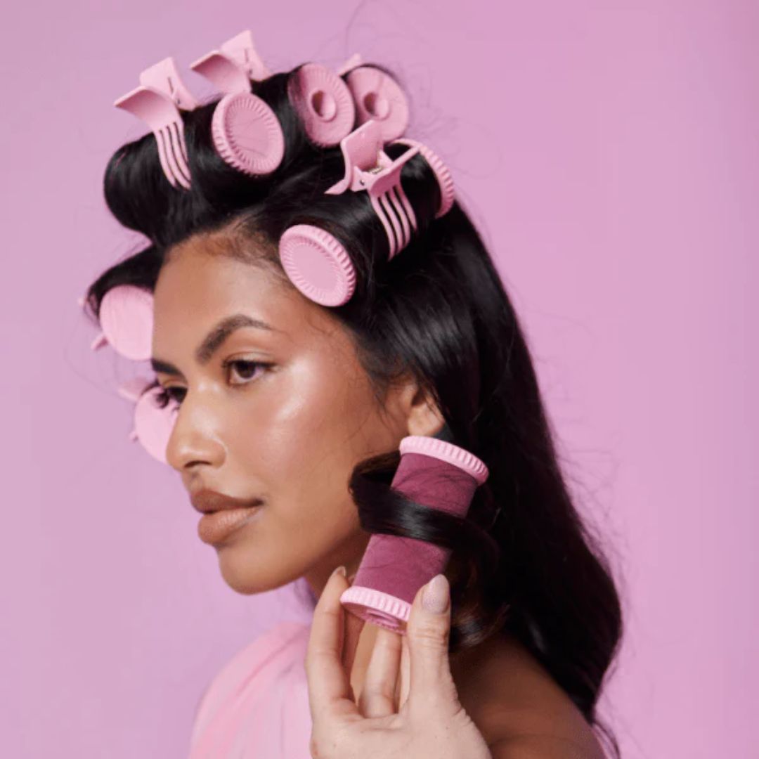 Woman using pink hair rollers against a pink background