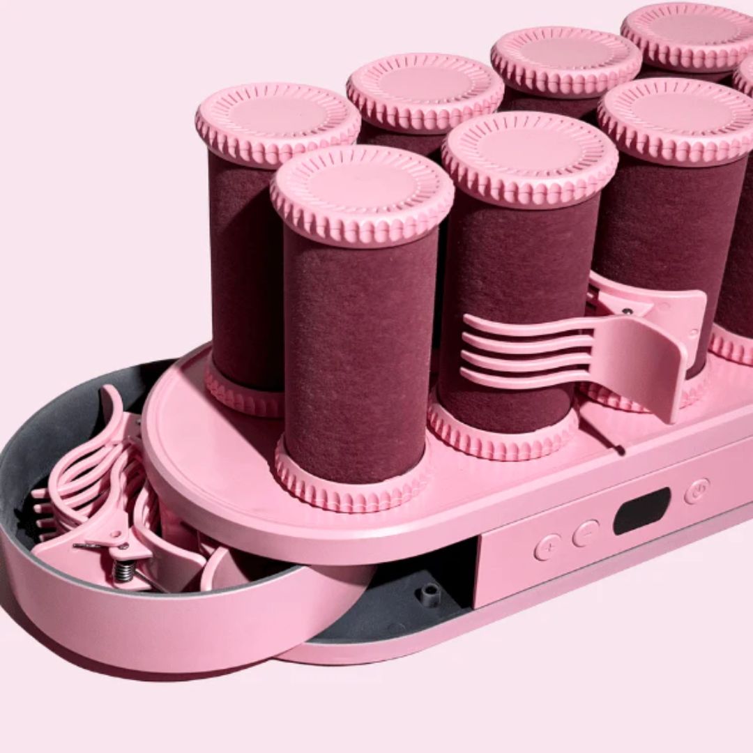 Pink hair roller set with multiple rollers and clips on a white background