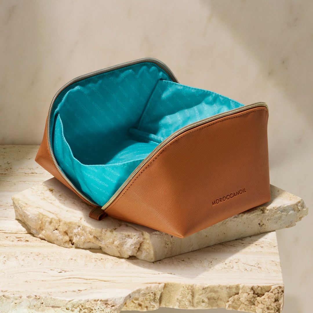 Brown leather toiletry bag with teal interior on a stone surface