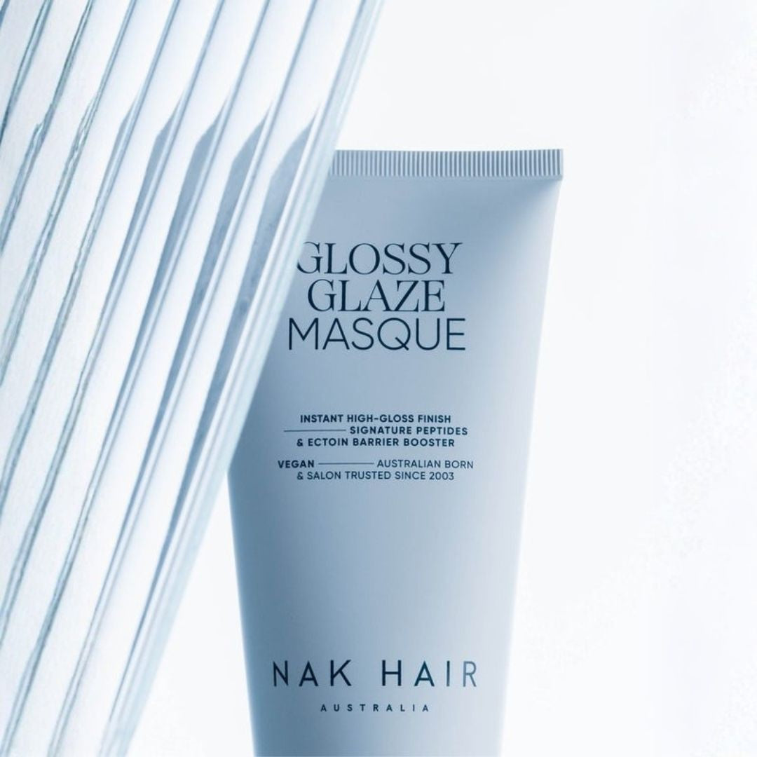 A light blue squeeze tube of NAK HAIR Glossy Glaze Masque hair product, standing upright against a bright white background with diagonal glass-like lines on the left.