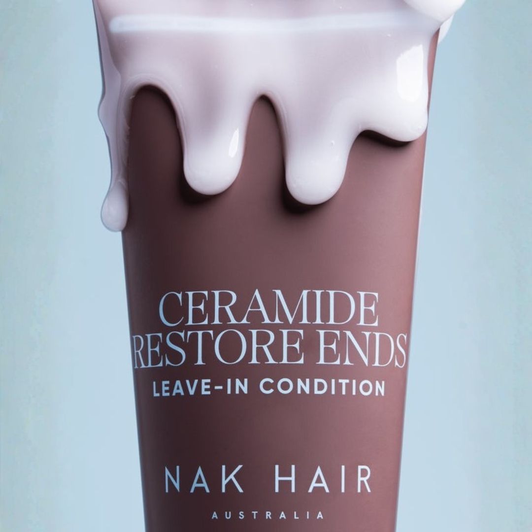 A close-up of a cosmetic tube labeled 'CERAMIDE RESTORE ENDS LEAVE-IN CONDITION' and 'NAK HAIR AUSTRALIA,' with a glossy mauve-brown body and white dripping cream at the top, on a pale blue background.