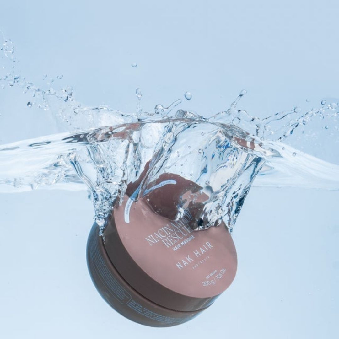 A jar of Nucleus Result N/AK Hair hair mask is shown mid-splash in clear water against a light blue background.