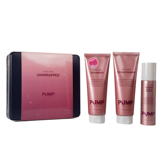 Pump Cosmetics Curl Hair Unwrapped set featuring a pink and black tin box alongside three matching pink haircare tubes: shampoo, conditioner, and a curl spray, all on a plain white background.