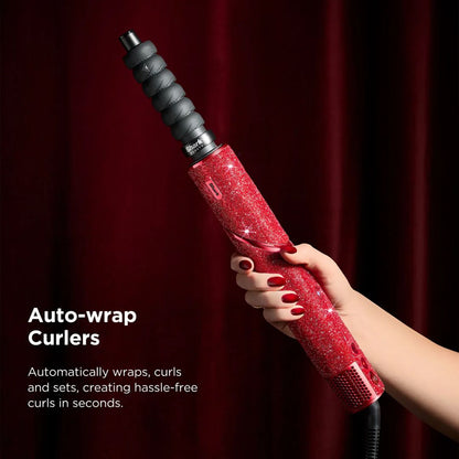 Red auto-wrap curler held by a hand with red nail polish against a dark background