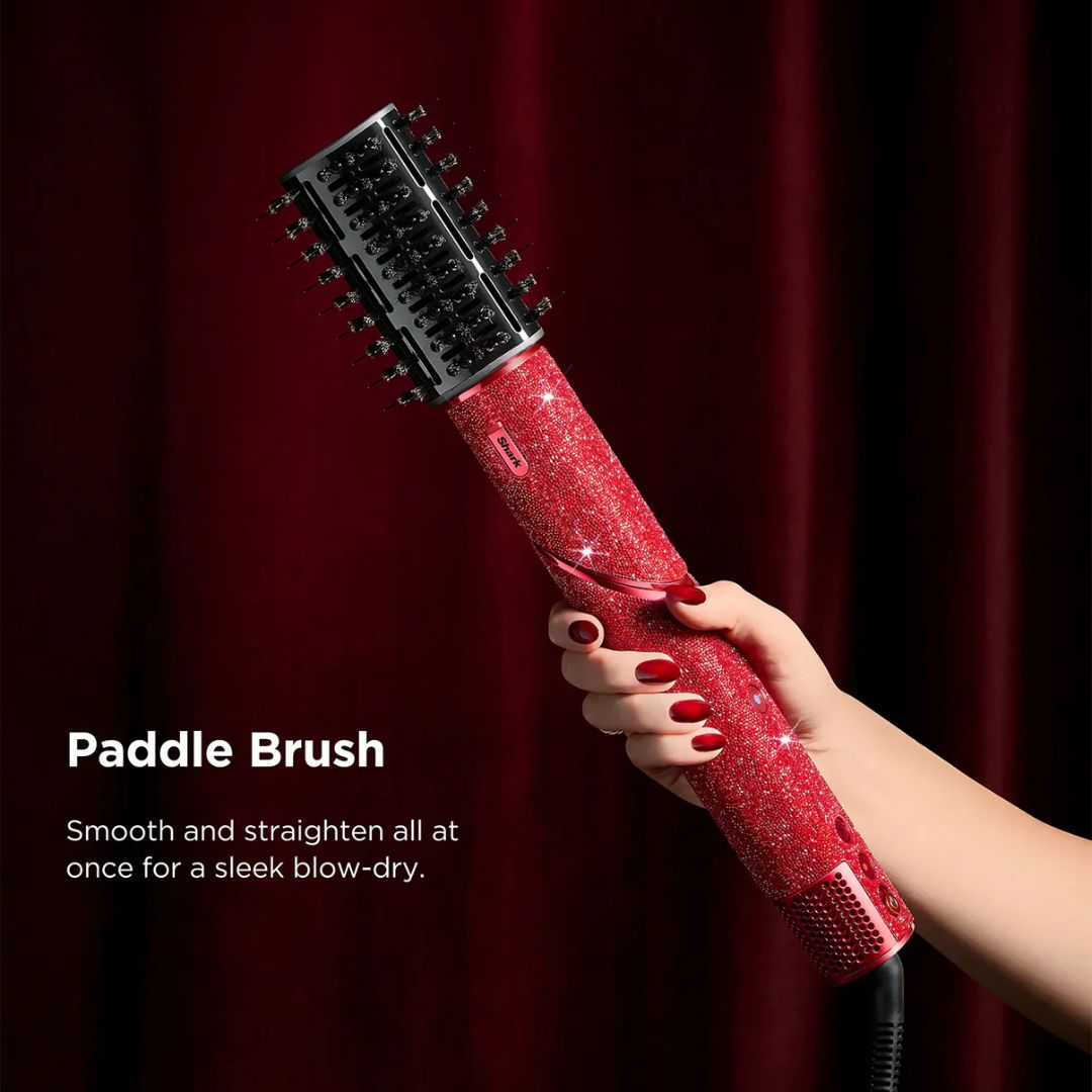 Red paddle brush with a hand holding it against a red curtain background