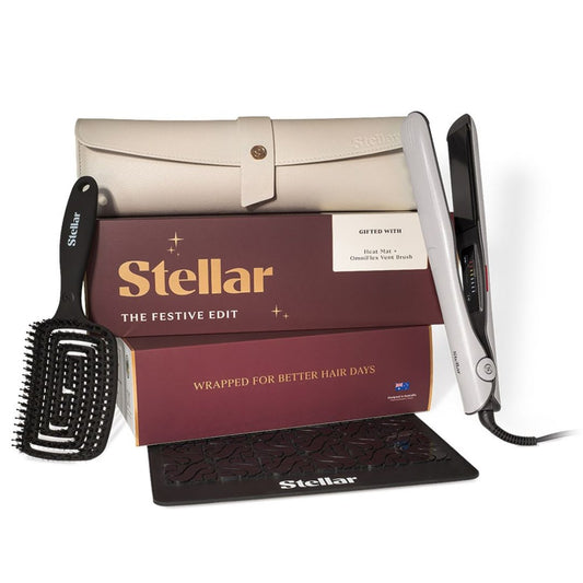 Stellar The Festive Edit hair care gift set featuring a silver flat iron, black paddle brush, black comb guard, and cream-colored storage case, arranged in front of branded burgundy and gold packaging boxes on a white background.