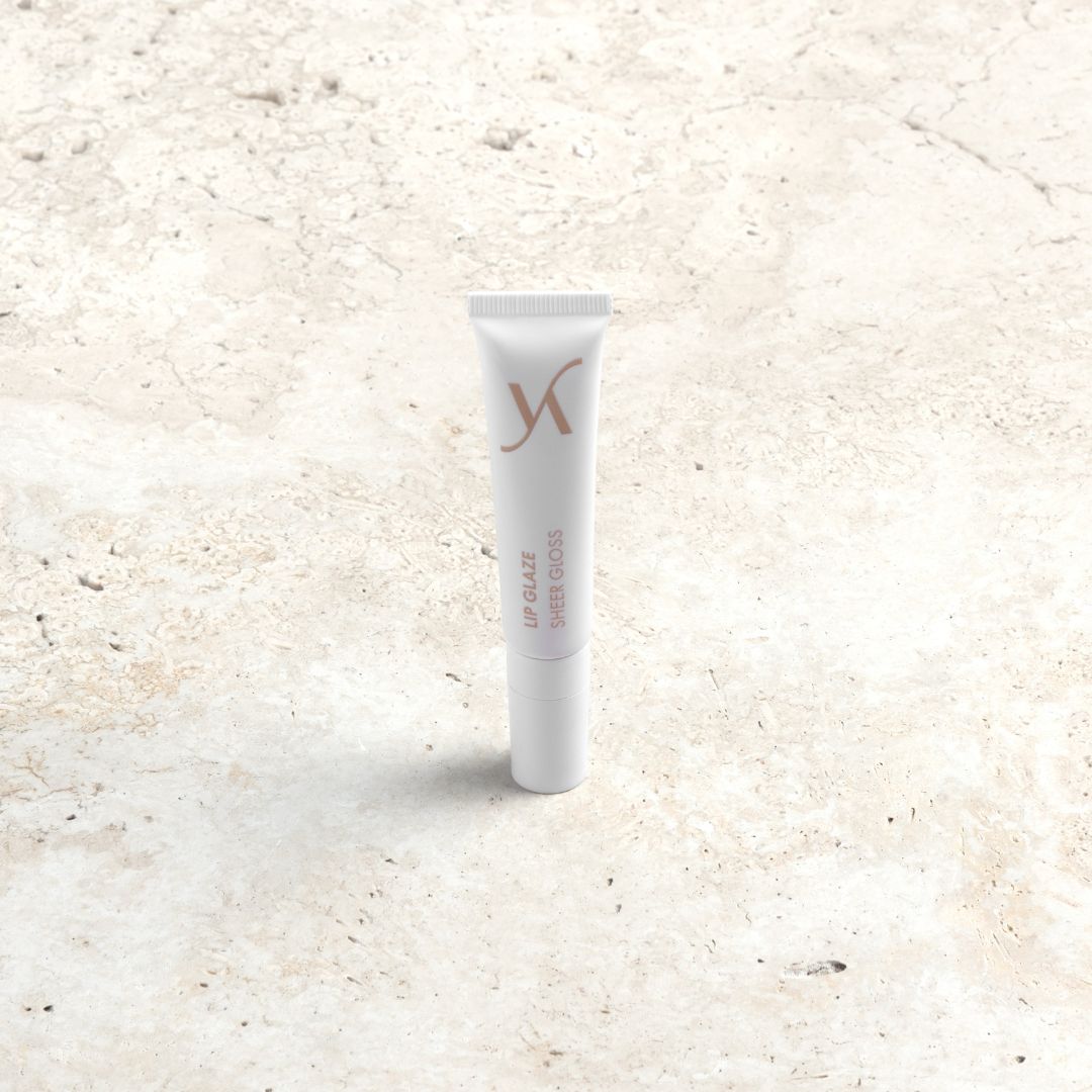 A white squeeze tube of Xylitol Lip Glaze Super Gloss standing upright on a light beige textured stone surface.