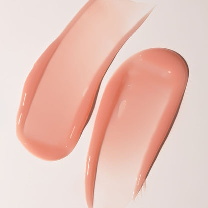 Two glossy swatches of a peachy pink cosmetic cream or liquid makeup on a clean white background.