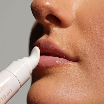 Close-up of a person applying a glossy lip balm or lip gloss from a white tube with a rounded applicator tip to their lips.