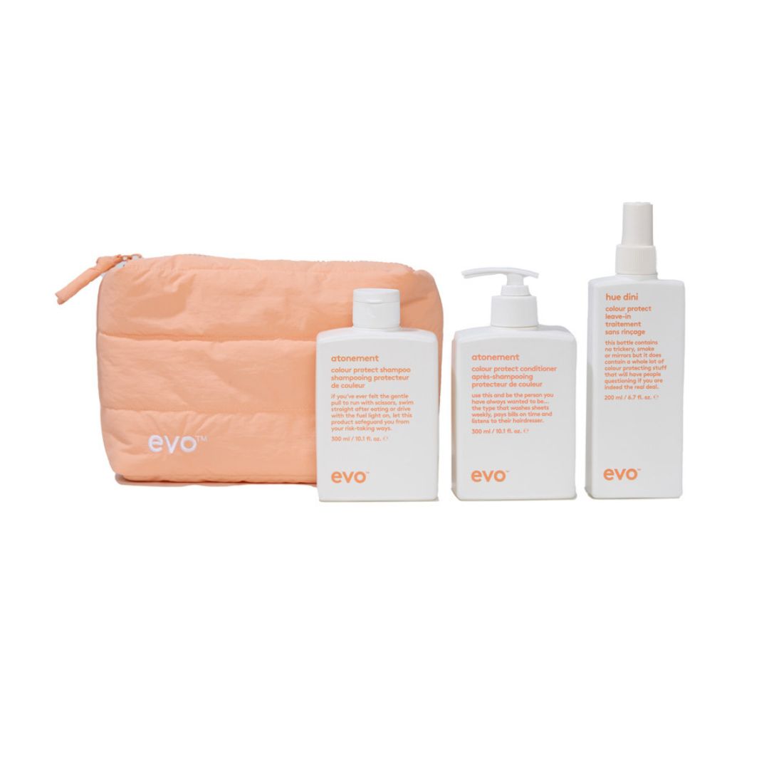 A 3-piece EVO hair care set with a peach zippered pouch, a white shampoo bottle, a white conditioner pump bottle, and a white hair oil spray bottle, all on a white background.