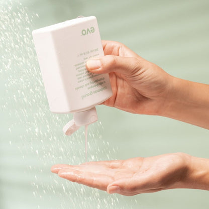Hand holding a white bottle labeled 'EVO' over another hand with water droplets on a light green background