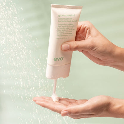 Hand holding a pink tube of 'ground control' hair product with a light green background