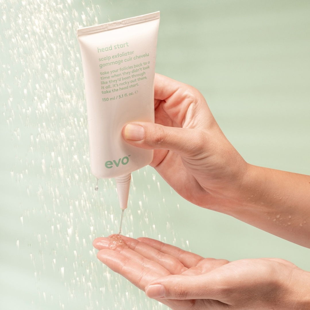 Hand holding a tube of evo hair product with a light green background
