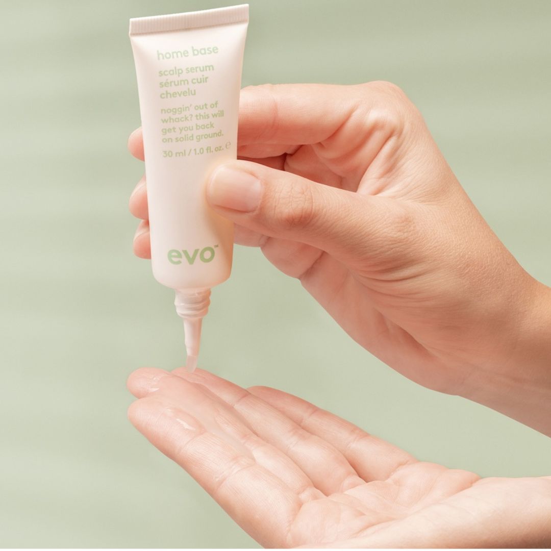Hand holding a tube of evo skincare serum with a light green background