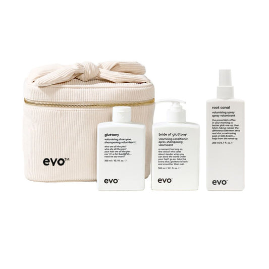 A set of three white EVO haircare bottles and a cream-colored zippered storage bag on a plain white background. The products include Glory shine shampoo, Bride of Gluttony volumining conditioner, and Root Canal volumining spray, with the brand name 'evo' printed in black on the bag and bottles.
