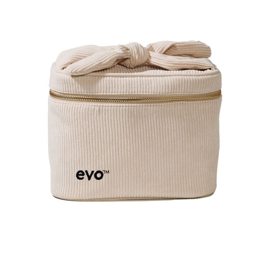 A cream-colored corduroy cosmetic bag with a top knot detail, a gold zipper, and the 'evo' brand logo printed in black on the front, set against a plain white background.