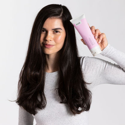 Woman holding a pink and white hair care product against a plain background