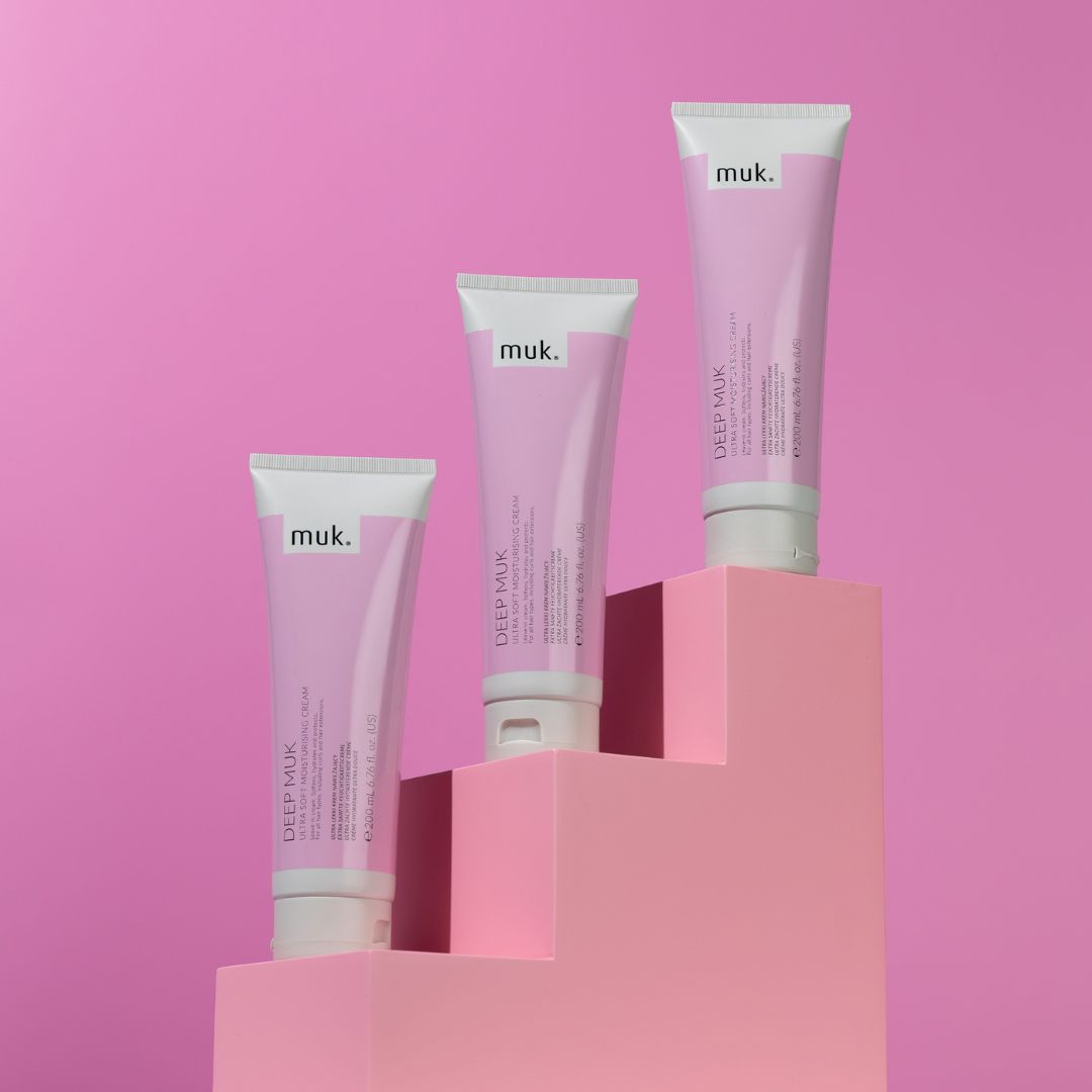 Three muk skincare products on pink platforms with a pink background