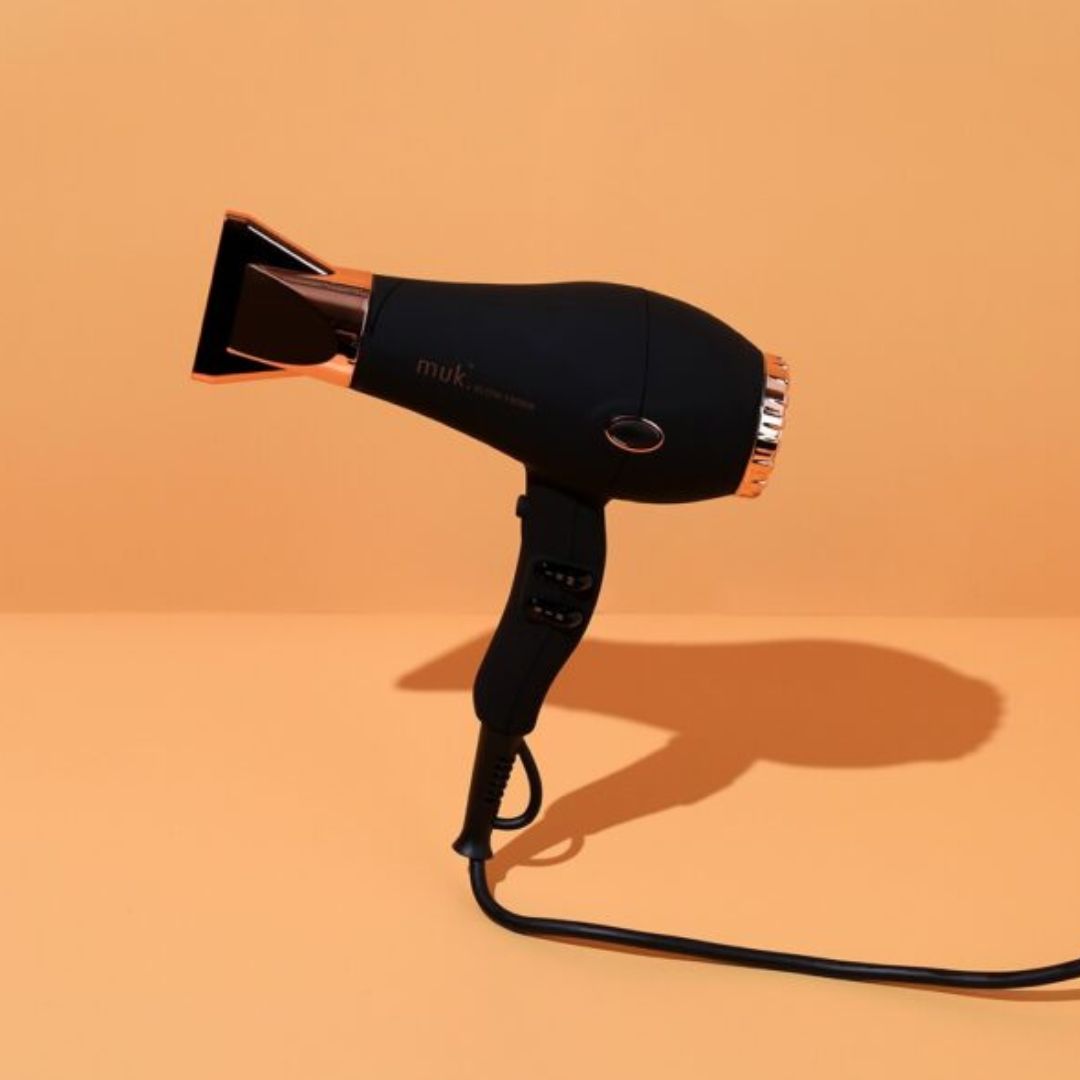 Black hair dryer with rose gold accents on a beige background