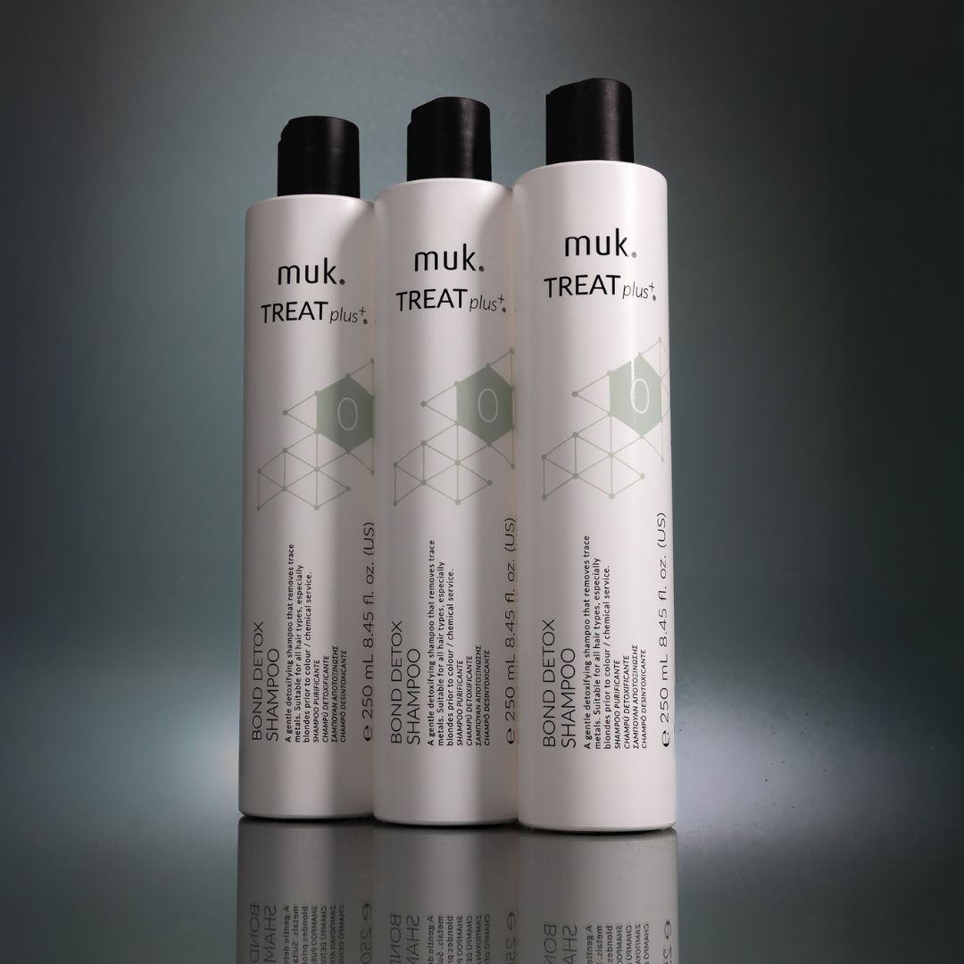 Three bottles of muk. Treat Plus Bond Detox Shampoo on a gray background