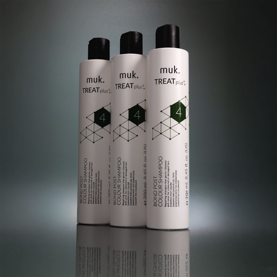 Three bottles of muk. TREAT plus+ shampoo on a reflective surface with a dark background
