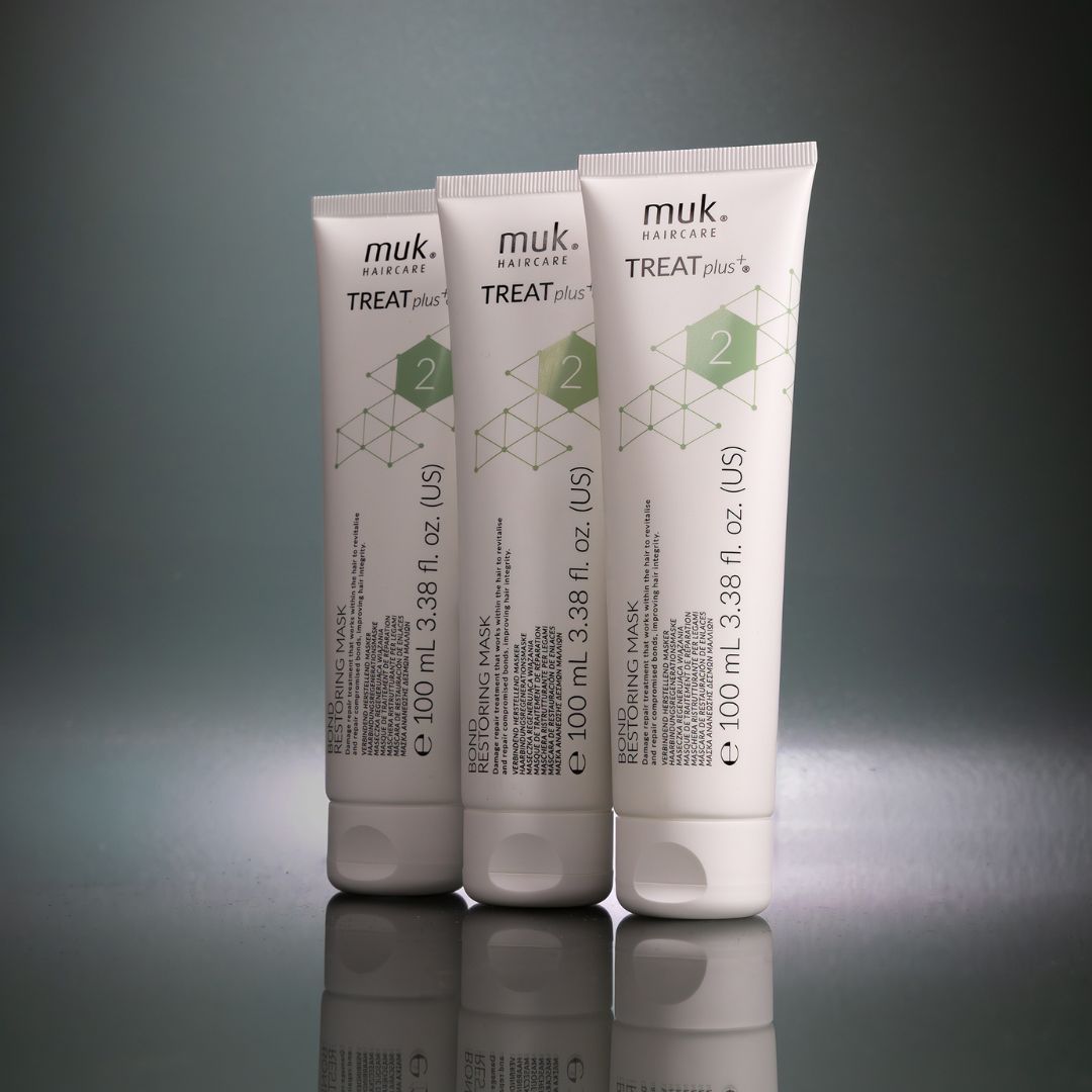 Three tubes of muk haircare Treat Plus mask on a reflective surface with a gray background